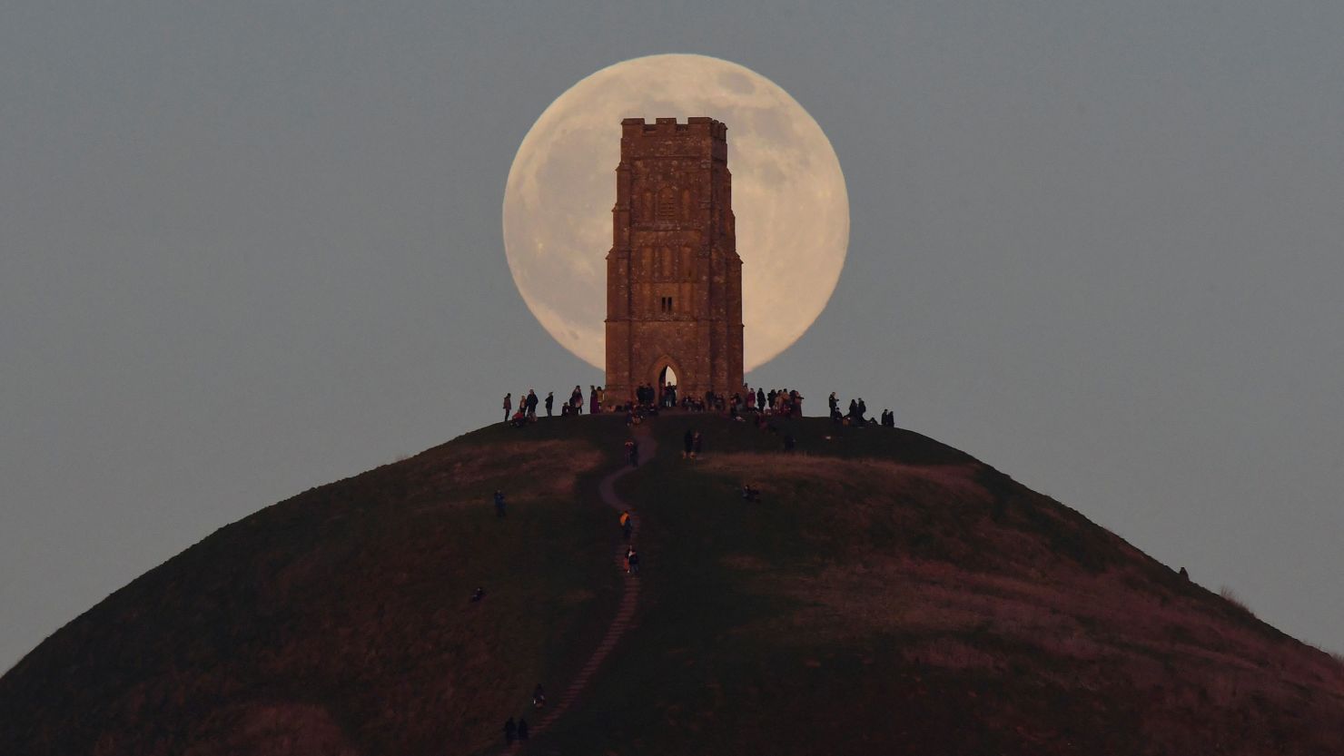 People stand beside St Michael's Tower as they watch the full moon, sometimes known as a "wolf moon," rise behind Glastonbury Tor in Glastonbury, England, on January 17.