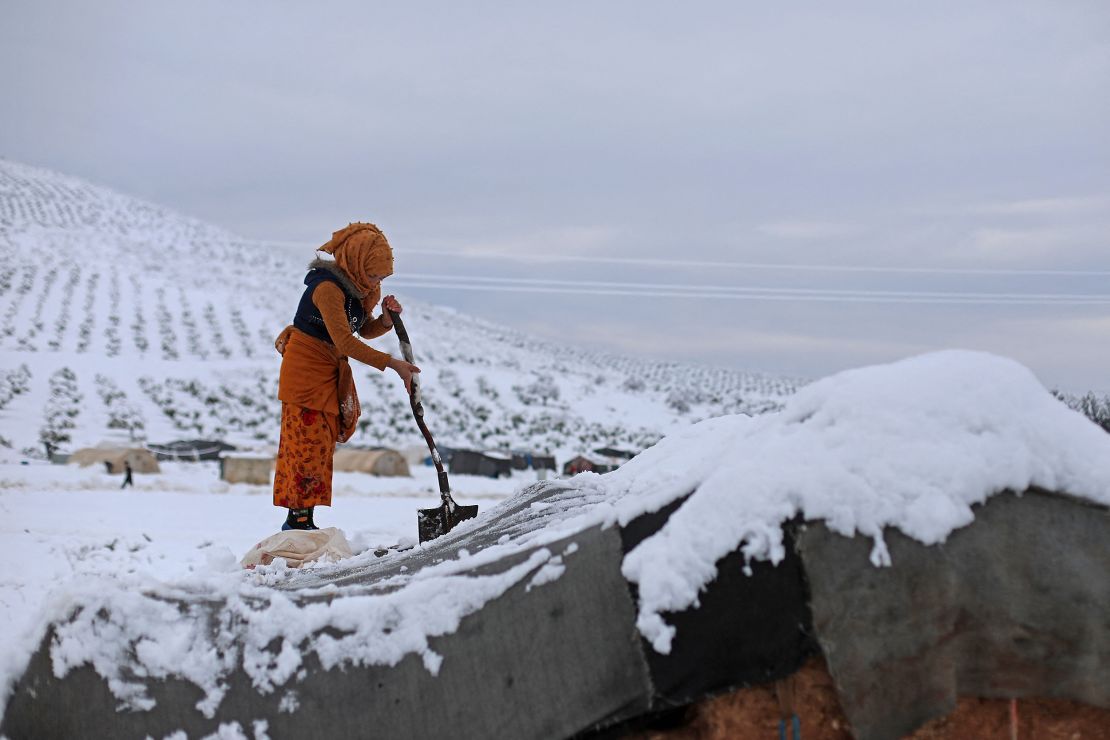 A woman shovels snow off her tent at a camp for internally displaced people in Raju, Syria.
