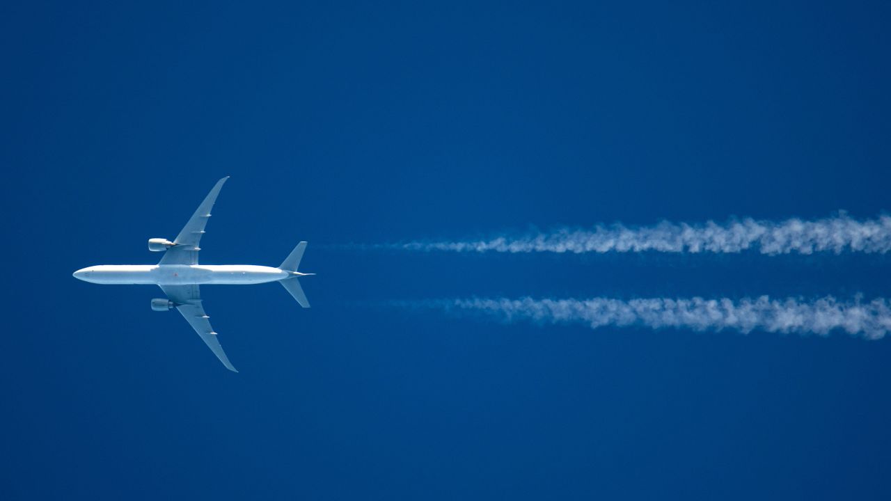 A white aircraft flying at 40.000 feet in the blue sky during a sunny day over Europe,  a flight during a clear winter day. The symbol illustration of the overflying wide-body jet airplane with no logo inscription print on the belly bottom of the fuselage is leaving behind contrails or condensation trail, a white vapor line. The aviation industry and passenger traffic is phasing a difficult period with the Covid-19 coronavirus pandemic having a negative impact on the travel business industry with fears of worsening situation due to the new Omega variant mutation. Eindhoven, The Netherlands on December 16, 2021 (Photo by Nicolas Economou/NurPhoto via Getty Images)