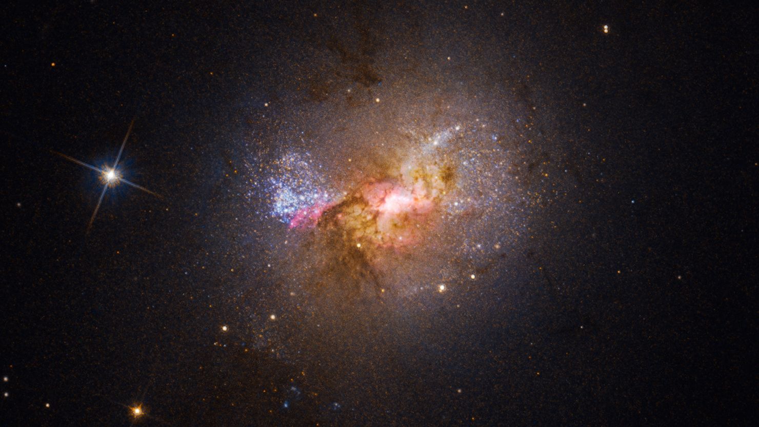 This Hubble Space Telescope image shows the dwarf galaxy Henize 2-10, which is filled with young stars. The bright center, surrounded by pink clouds, indicates the location of its black hole and areas of star birth.