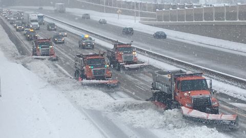 Snow plows line up, from the left side of the road to the right, clearing accumulated snow on a Minnesota highway.
