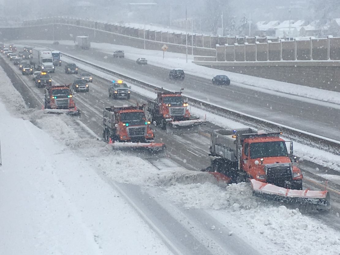 Snowplows line up, from the left side of the road to the right, plowing  accumulated snow on a Minnesota highway.