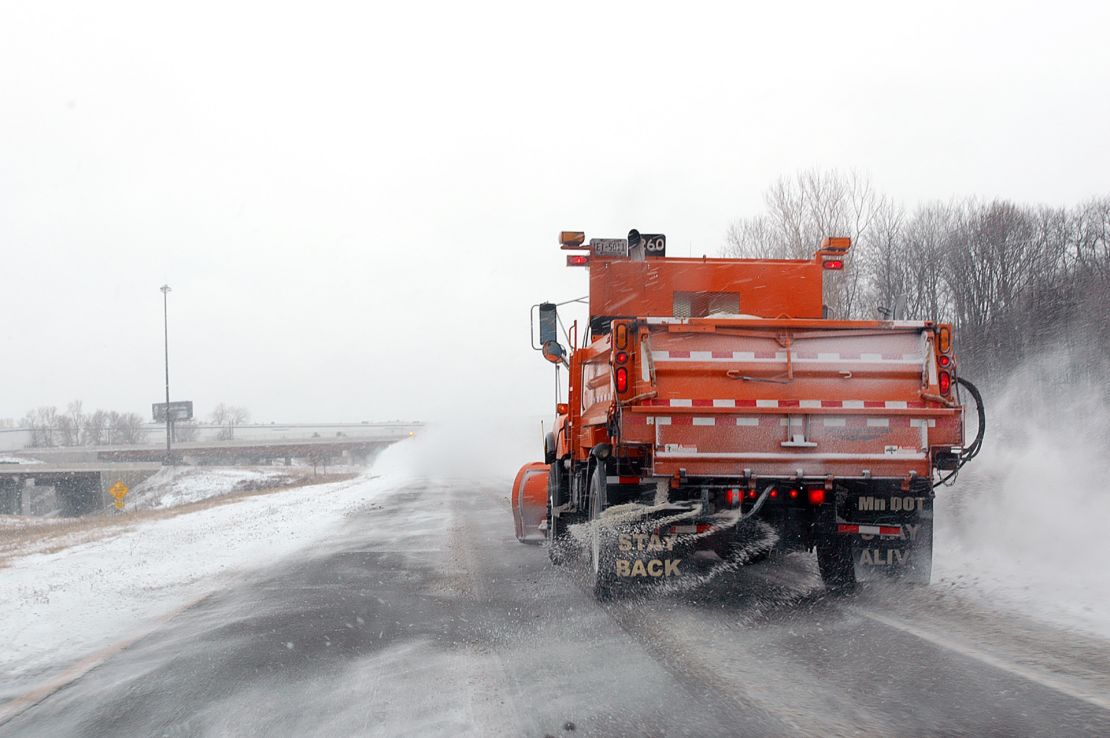A snowplow sprays salt on a frozen Minnesota highway.