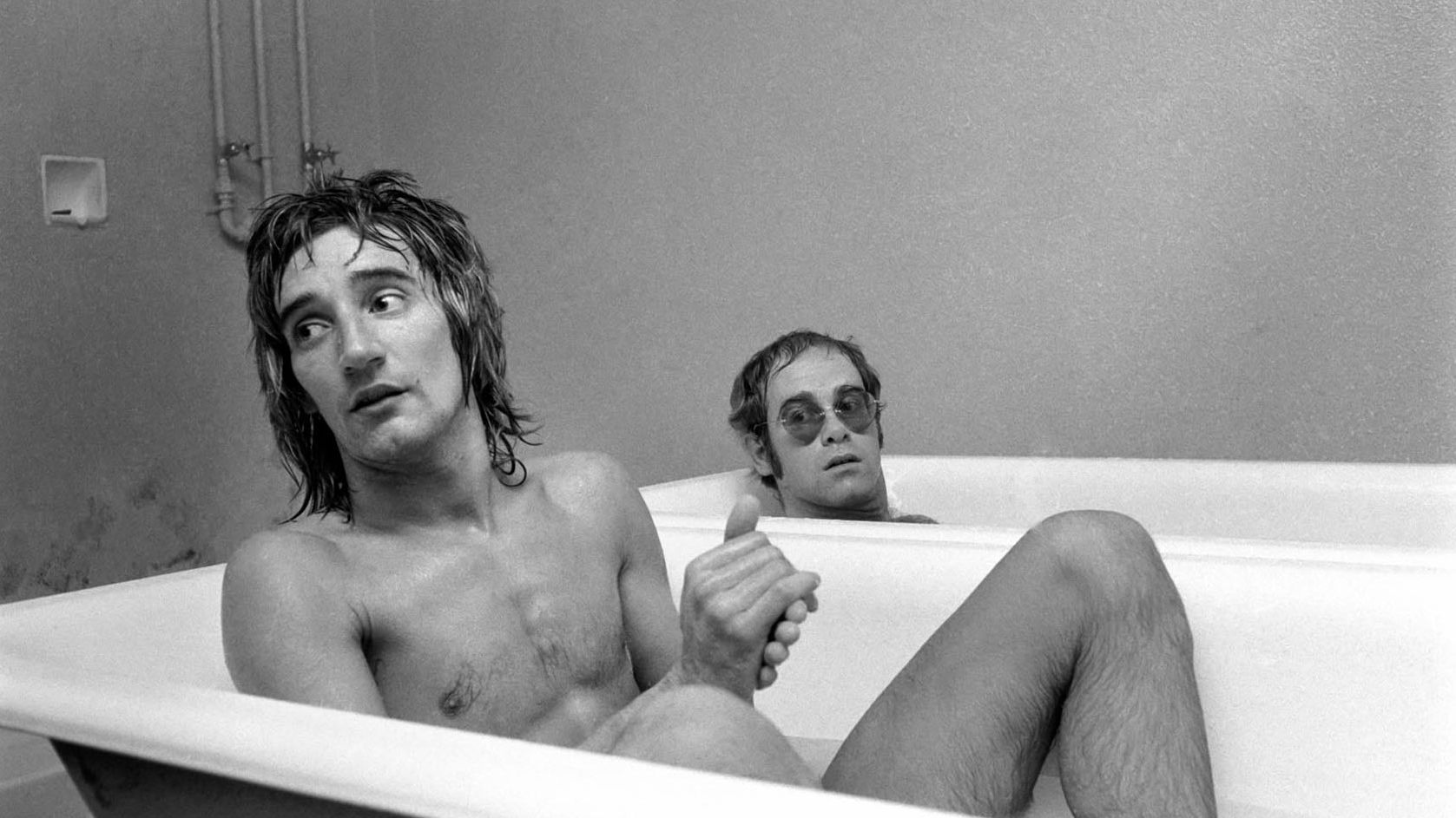 John and singer Rod Stewart have a bath at the stadium of Watford Football Club in 1973. John, a lifelong Watford fan, later owned the English soccer club. Today, one of the stadium's stands is named after him.