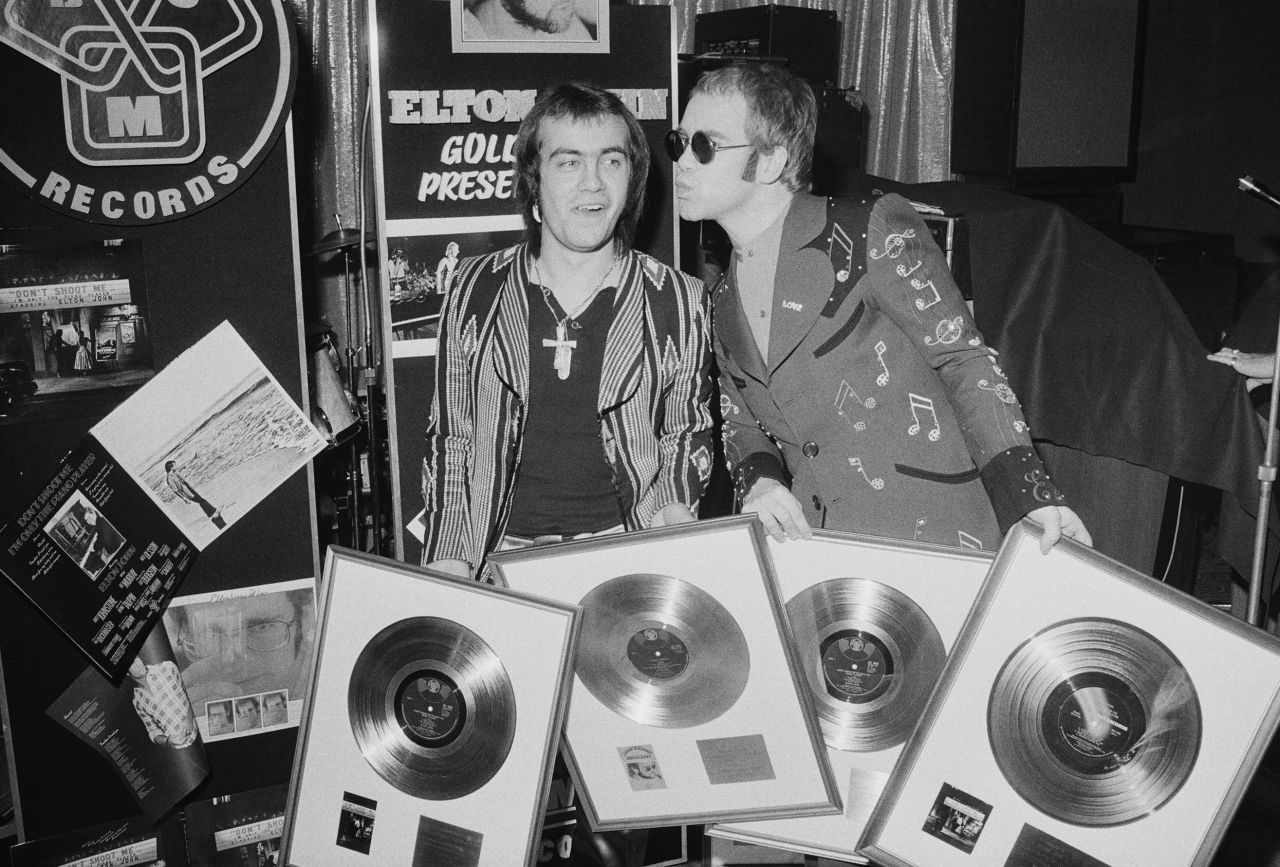 John and his songwriting collaborator, Bernie Taupin, hold gold records in 1973. Taupin has written the lyrics for many of John's songs over his career, and the two have worked together for decades.