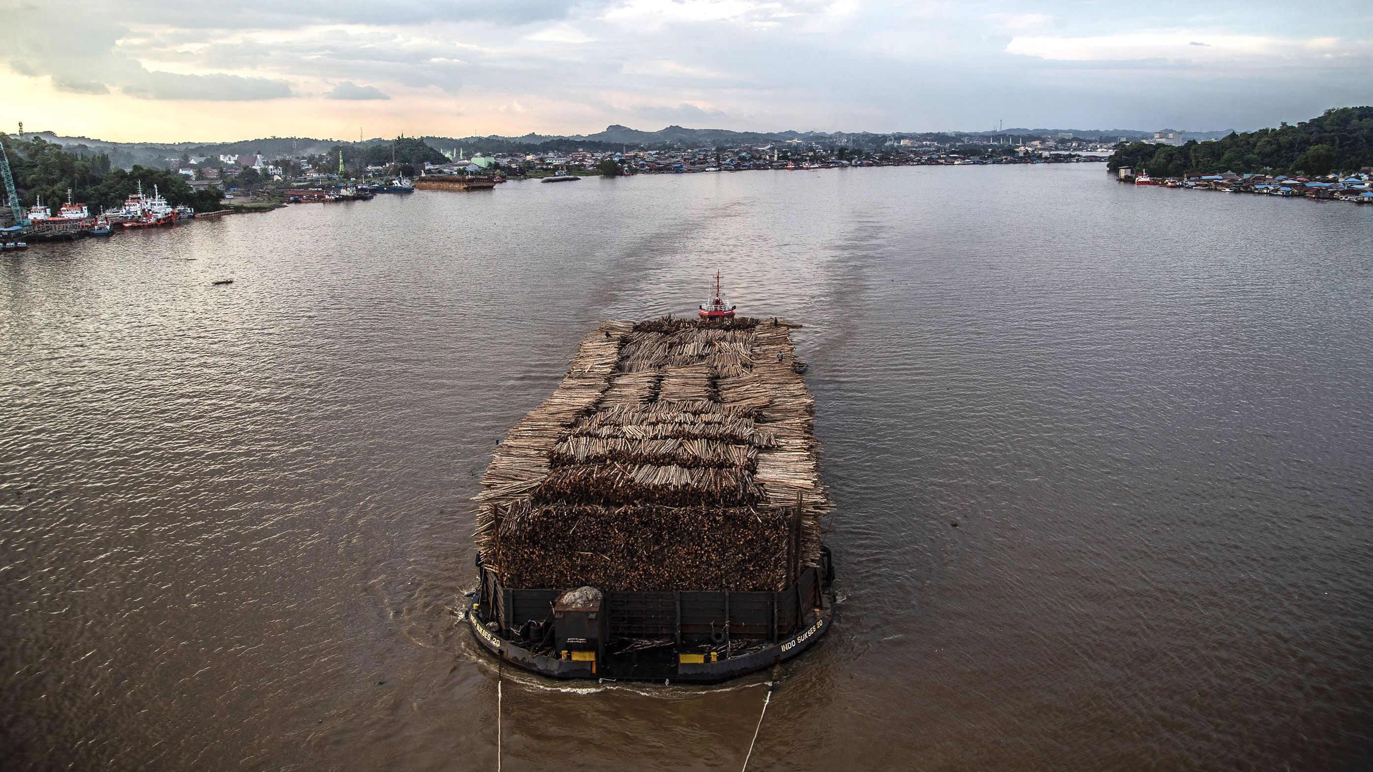 A barge filled with logged timber pulled along the Mahakam river passes the town of Samarinda, East Kalimantan on November 4, 2021. 