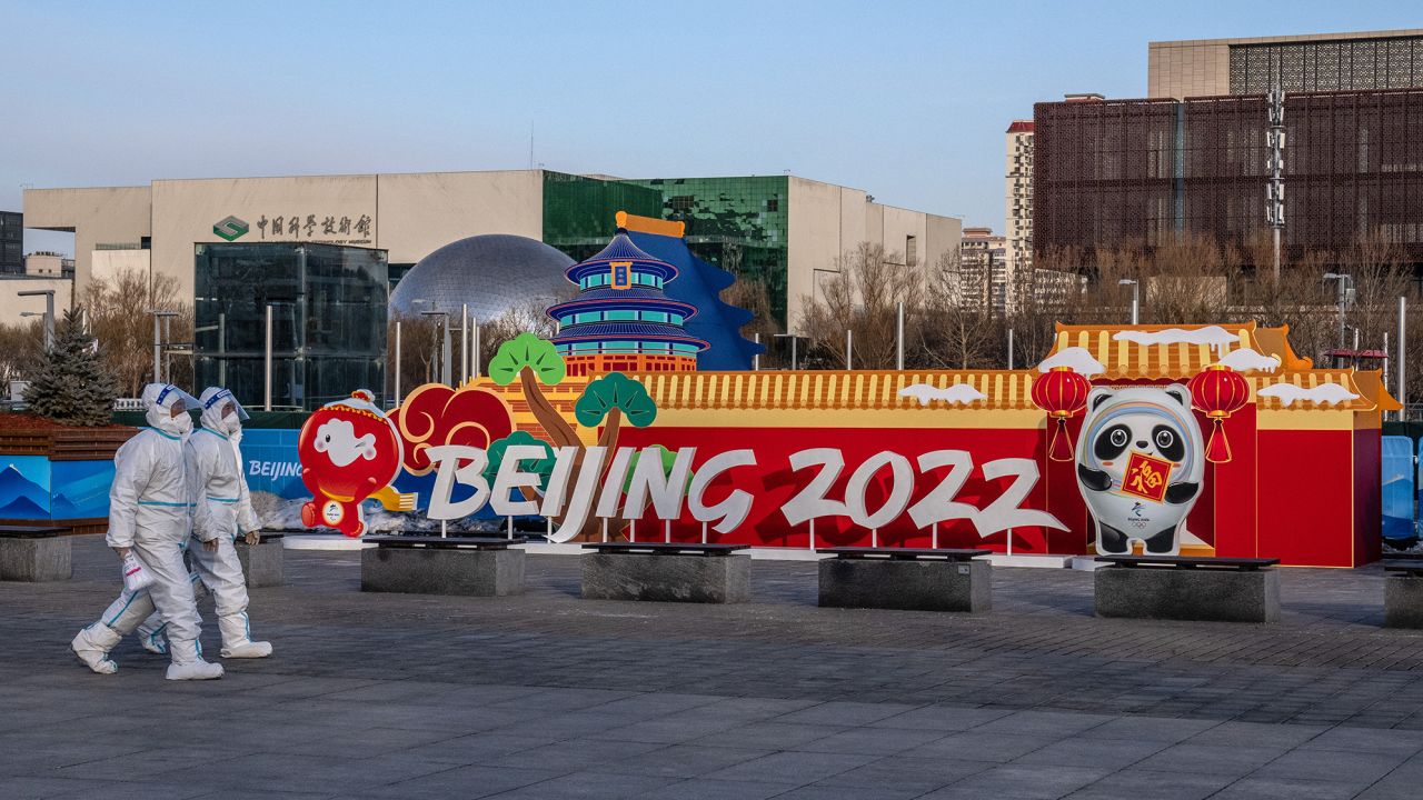 People in personal protective kits walking past a Winter Olympics display on Wednesday in Beijing.