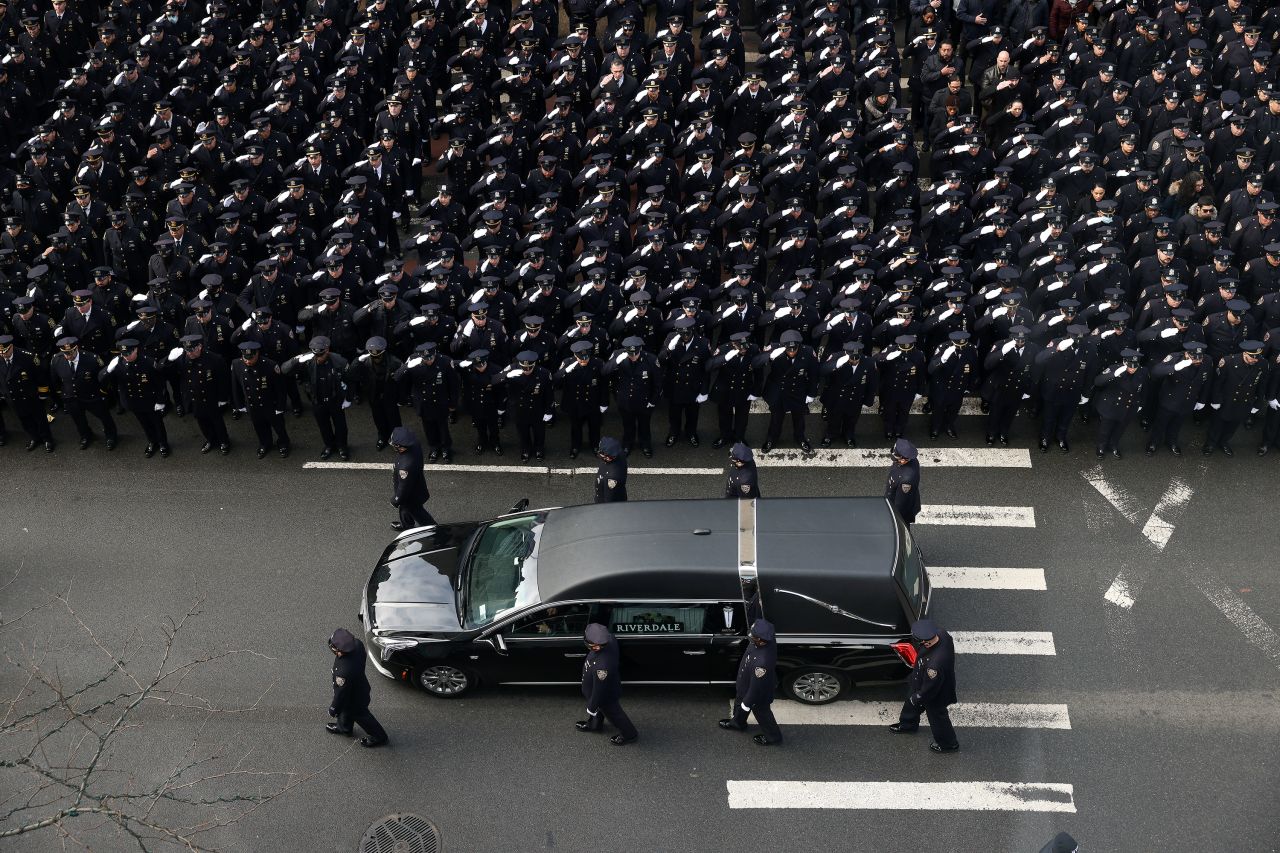 Police salute as a hearse carries Mora's casket down Fifth Avenue.