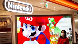 An employee wearing a face mask stands next to a screen displaying a character of Nintendo game Super Mario at a store for Japanese games giant Nintendo in Tokyo on February 3, 2022. (Photo by Behrouz MEHRI / AFP) (Photo by BEHROUZ MEHRI/AFP via Getty Images)