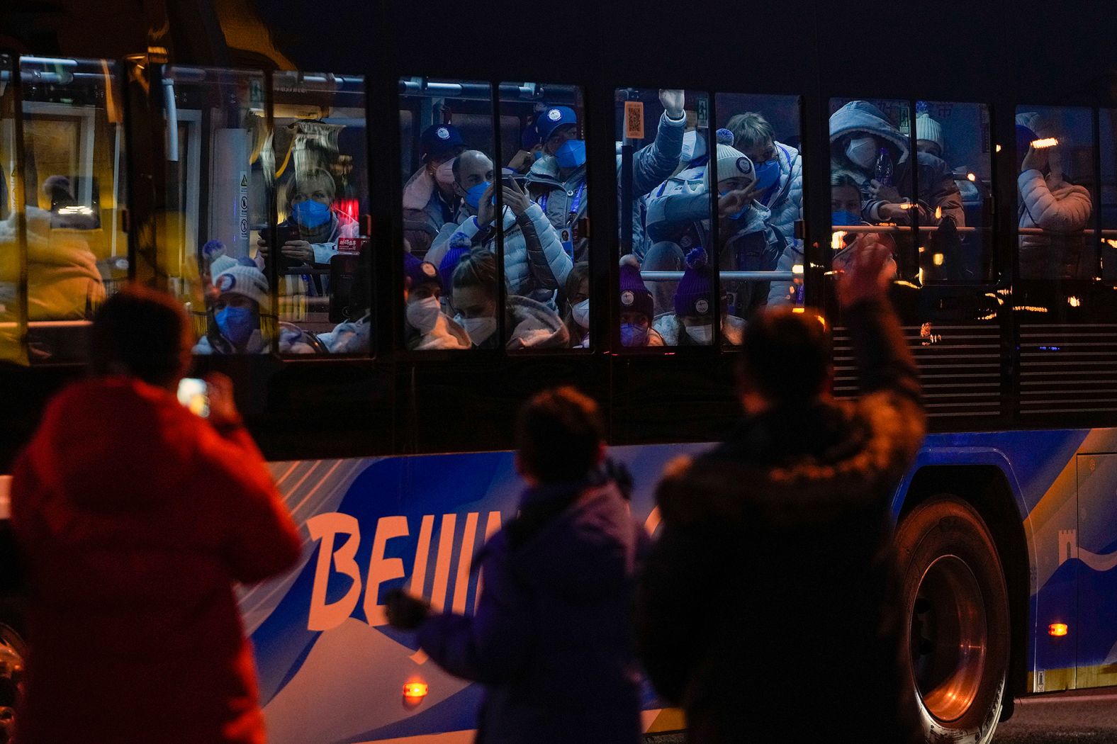 Athletes inside a bus wave to residents on the street as they head to the stadium for the opening ceremony.