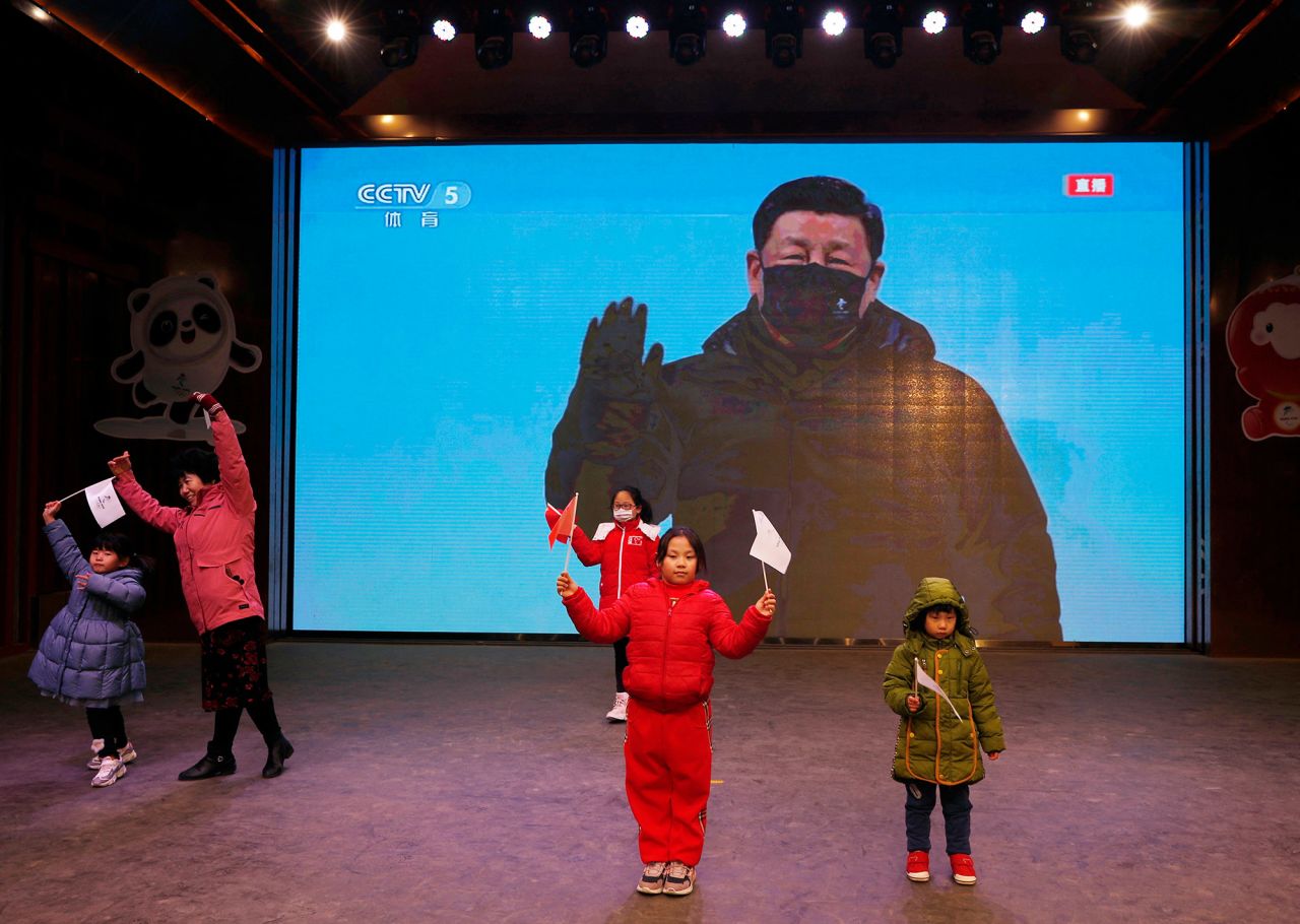 People pose for pictures in front of a giant screen showing Chinese President Xi Jinping as the opening ceremony is broadcast in Beijing.