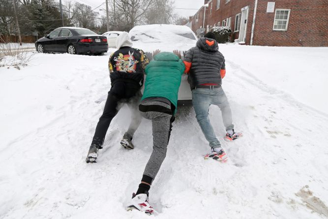 Three men work to push a car up a driveway in Columbus, Ohio.