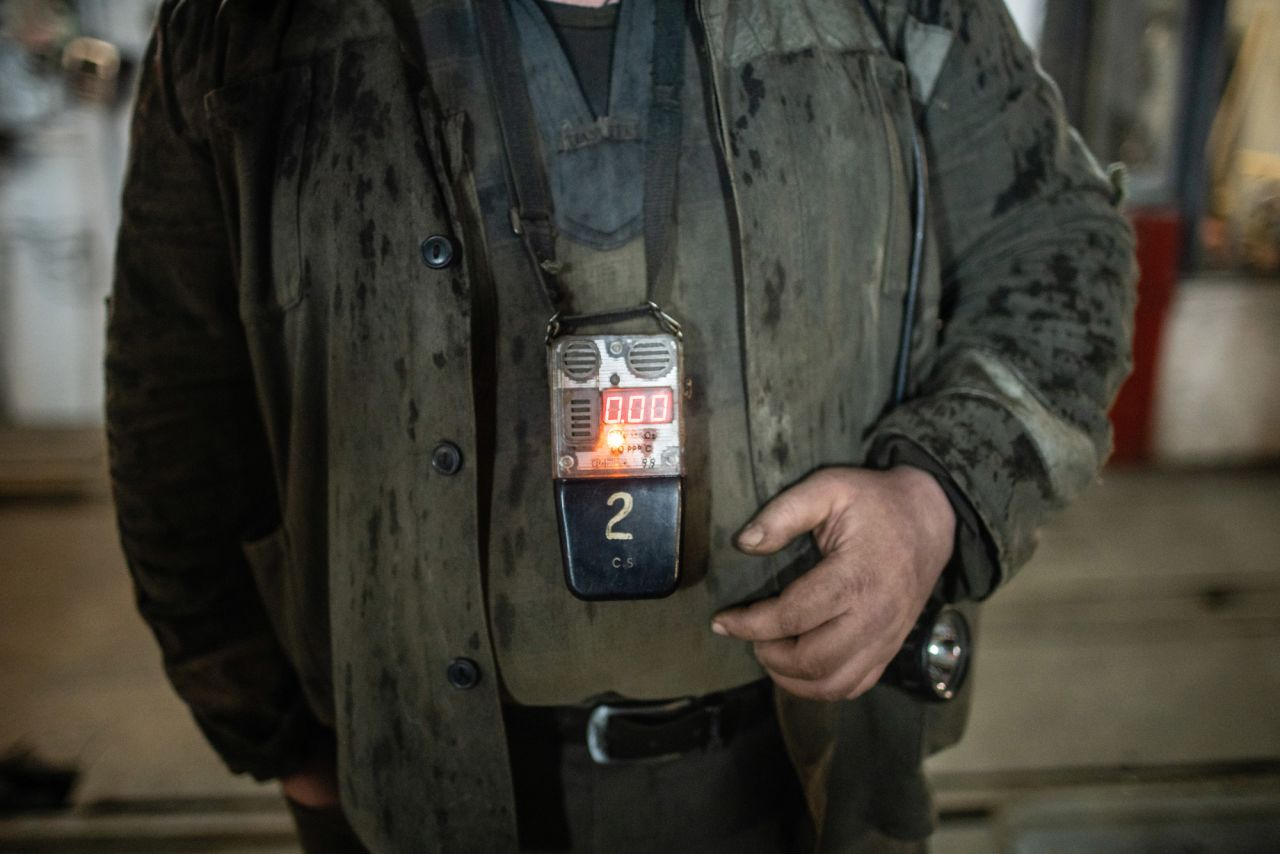 A miner wears a methane gas detector. The youngest miner at this site is 18 years old, and the oldest is 65.