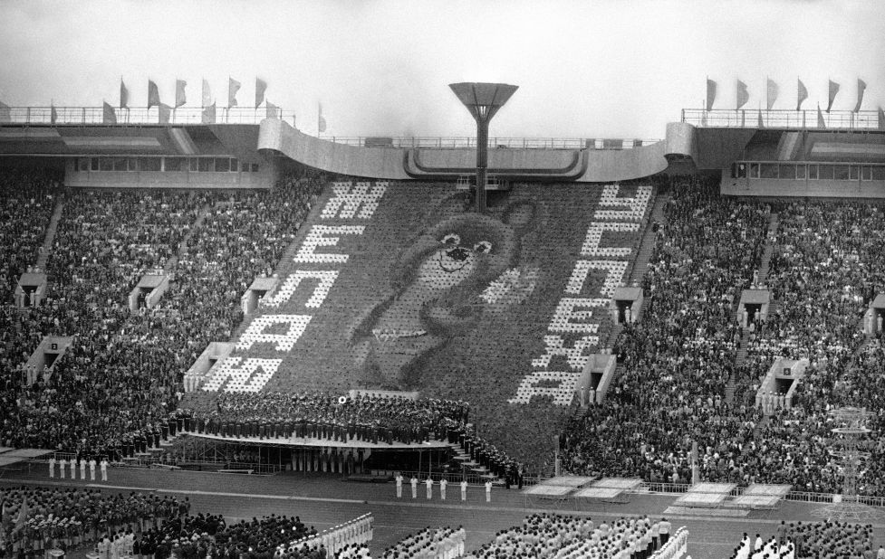 Card-bearing people form image of Misha, the Russian bear mascot of the 1980 Summer Olympic Games, flanked by the worlds, "Good Luck," in Russian during opening ceremonies of the games in Moscow's Lenin Stadium.