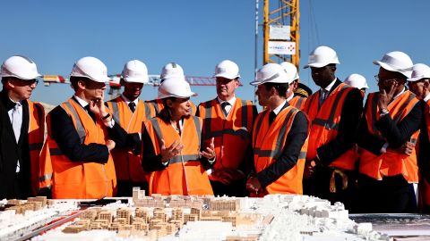 Paris Mayor Anne Hidalgo (C) speaks past French President Emmanuel Macron (second L) during a visit of the building site of the Olympic Village in Saint-Ouen on October 14, 2021.