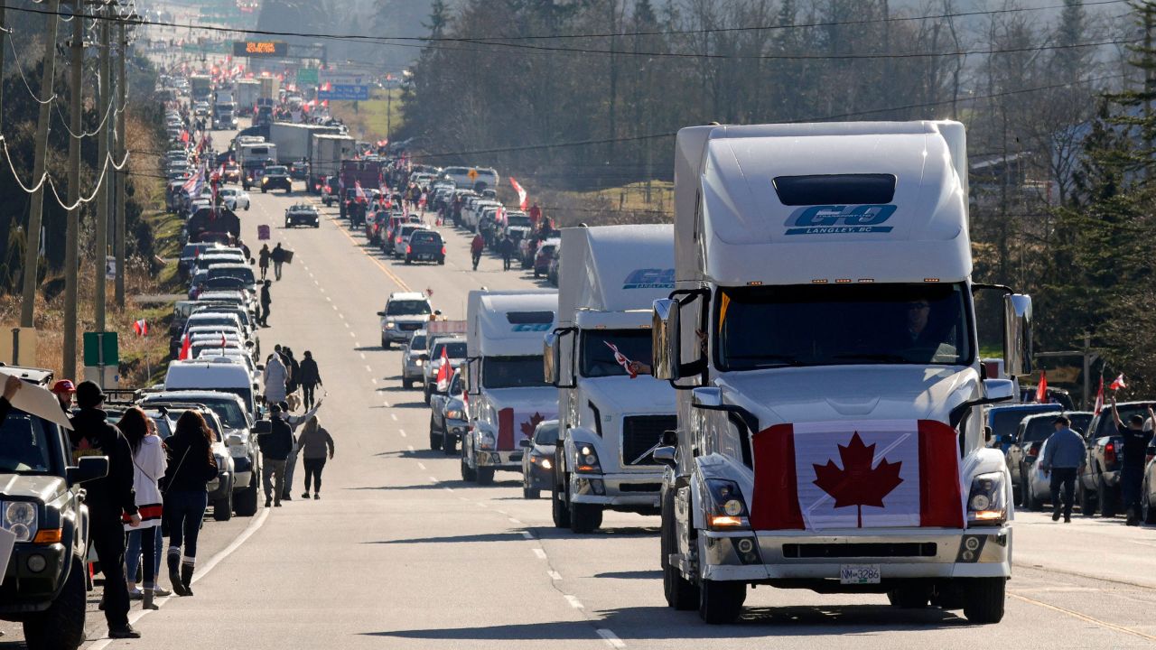 Trucks with Canadian flags drive by anti-vaccine mandate and anti-government protesters Saturday in Surrey, British Columbia, near the border with Washington state. 