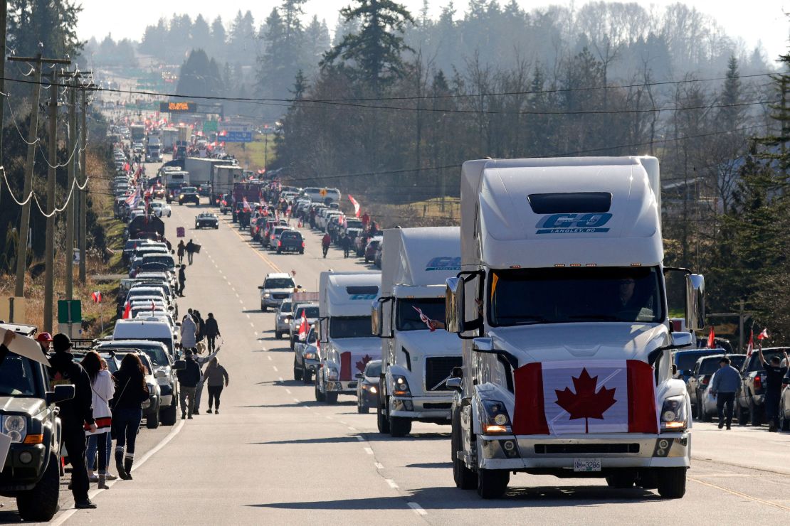 Trucks with Canadian flags drive by anti-vaccine mandate and anti-government protesters Saturday in Surrey, British Columbia, near the border with Washington state. 