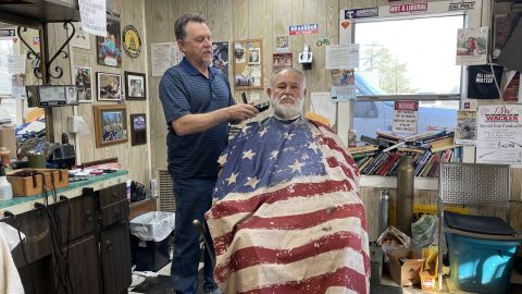 Woody Clendenen drapes his customers in a US flag cape before cutting their hair in his barber shop.