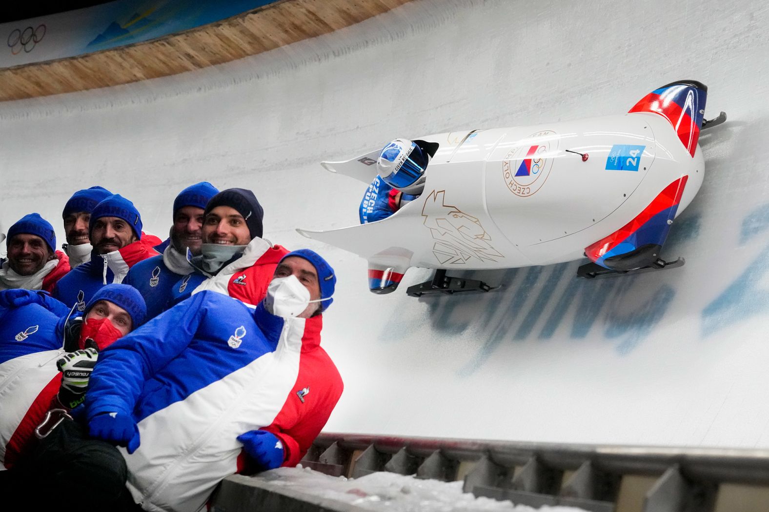 Members of the Czech Republic team pose for a photo as teammates Dominik Dvorak and Jakub Nosek slide past in a bobsled on Monday, February 14.