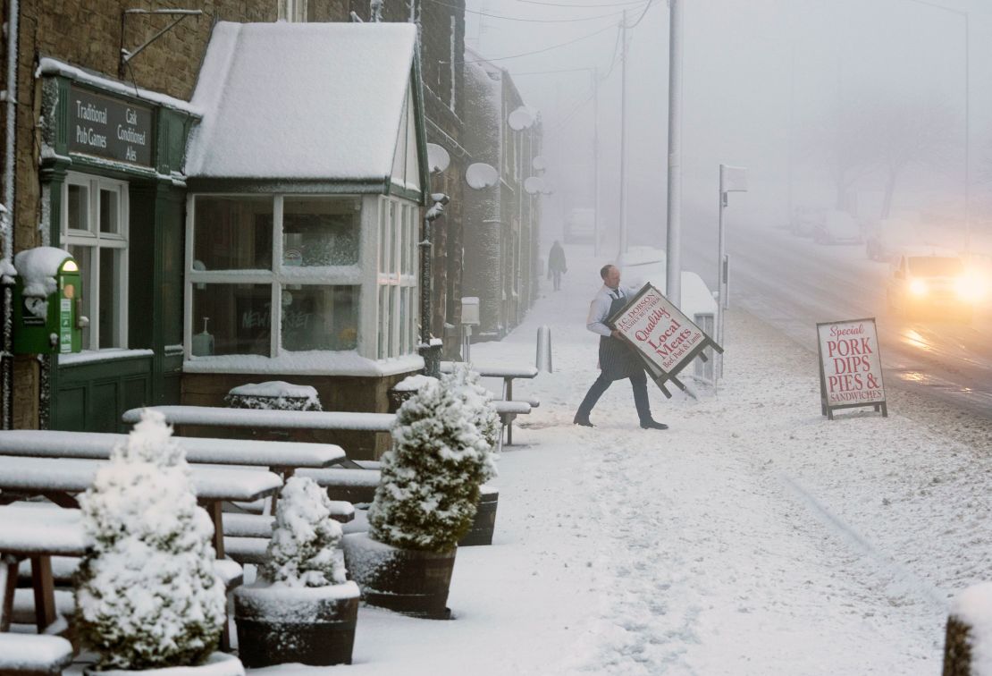 A local butcher carries his shop sign across a snowy pavement in  County Durham, Britain, as Storm Eunice makes landfall.