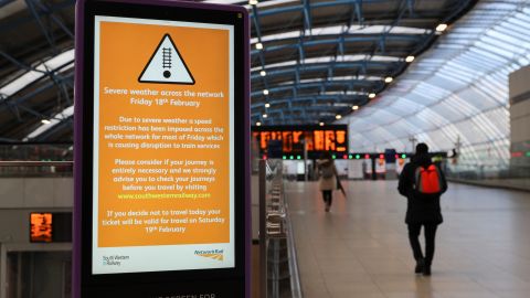 A person walks past a sign at Waterloo station, warning of severe weather. 
