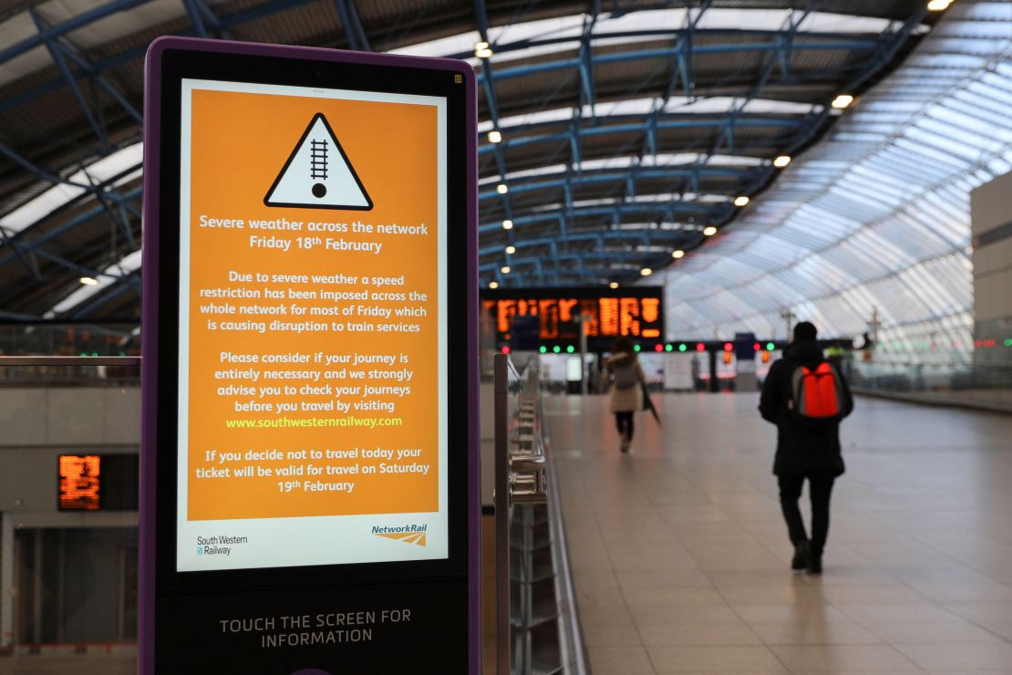 A person walks past a sign at Waterloo station, warning of severe weather. 