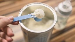 Powder milk for baby and blue spoon on light background close-up. Milk powder for baby in measuring spoon on can. Powdered milk with spoon for baby. Baby Milk Formula and Baby Bottles. Baby milk formula on kitchen background