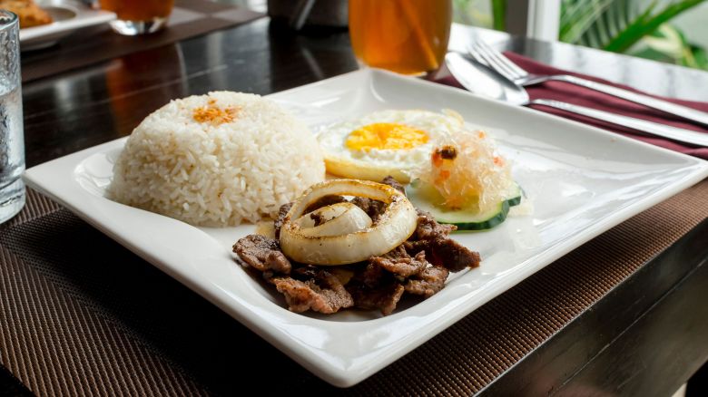 A serving of Tapsilog served with garlic rice,sunny side egg, atchara and cucumber slices. Topped with onion.
