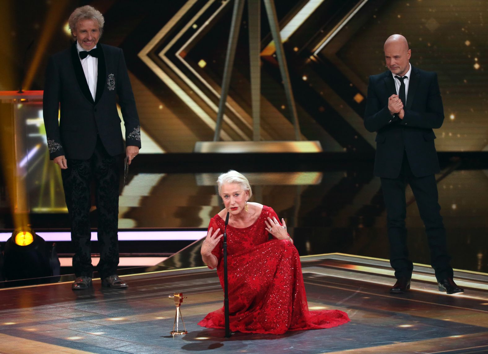 Mirren kneels on stage between Thomas Gottschalk, left, and Christian Berkel at the Golden Camera Awards in Hamburg in 2016.