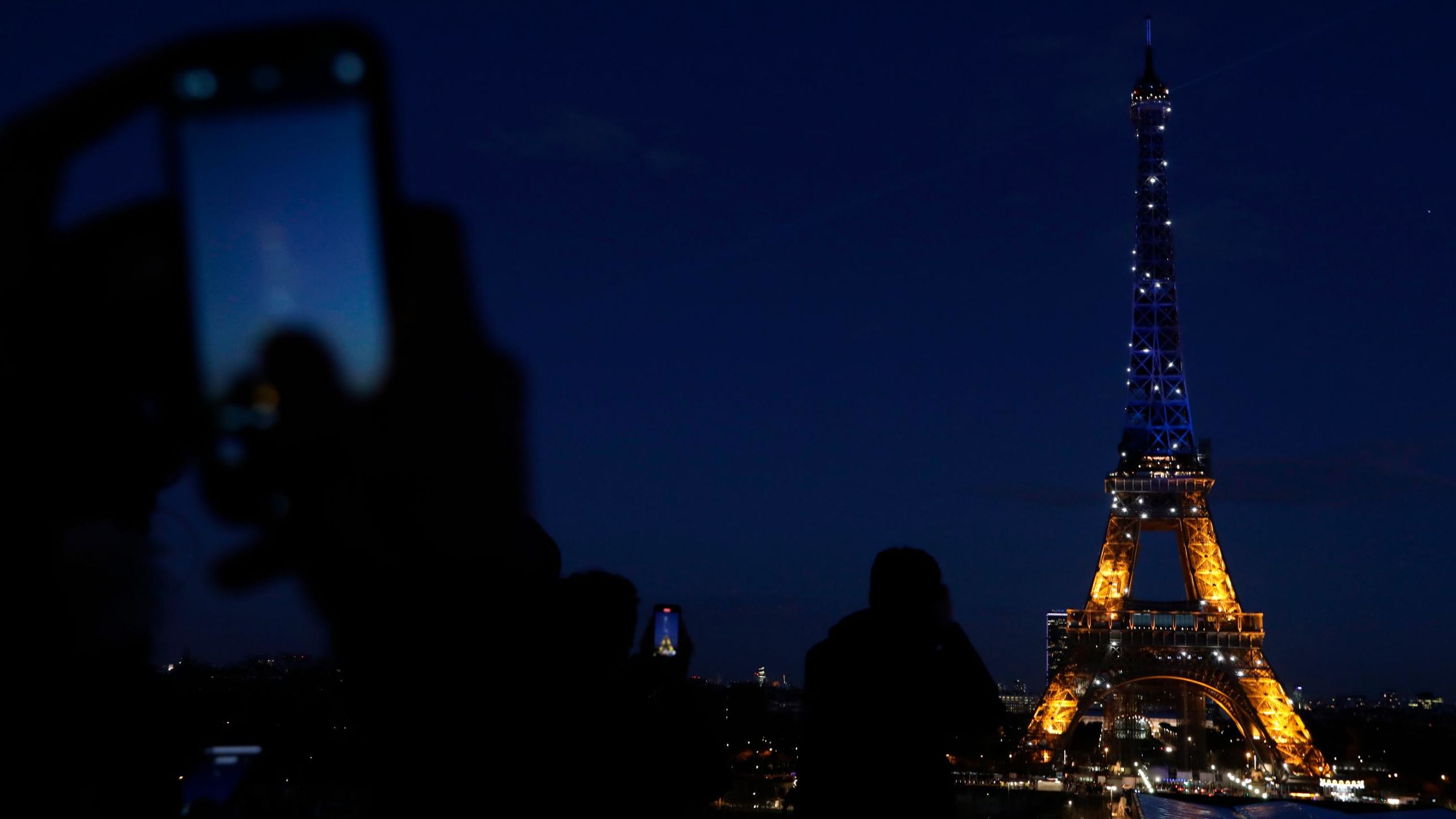 People photograph Paris' Eiffel Tower as it is lit with Ukraine's colors on February 25.