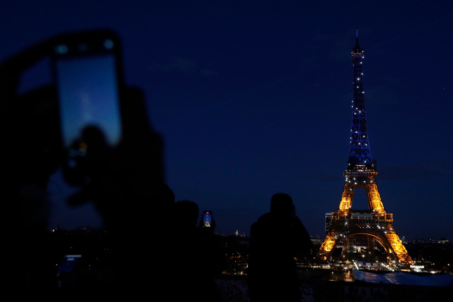 People photograph Paris' Eiffel Tower as it is lit with Ukraine's colors on February 25.