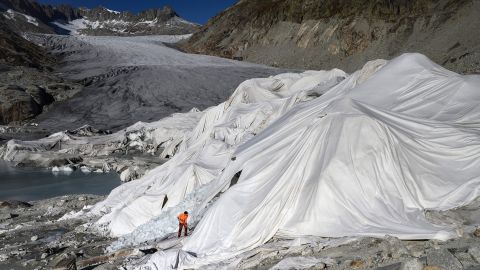 A man works in the Swiss Alps at the Rhone Glacier in October 2021, which is partially covered with insulating foam to prevent it from melting due to global warming.