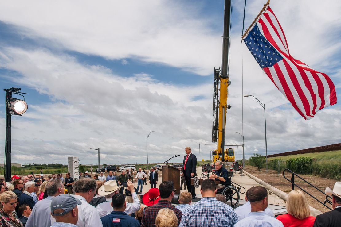 People listen to Texas Gov. Greg Abbott's address, during a tour to an unfinished section of the border wall with former President Donald Trump on June 30, 2021 in Pharr, Texas. 