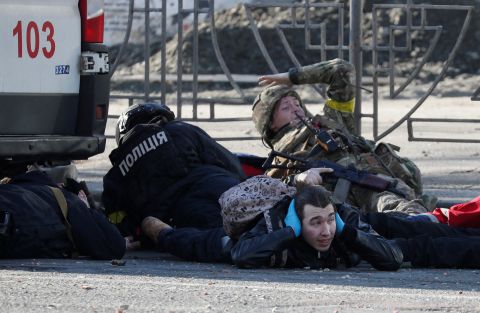 People in Kyiv take cover as an air-raid siren sounds February 26 near an apartment building that was damaged by shelling.