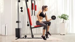 Female exercising with a dumbbell and sitting on a fitness machine at home