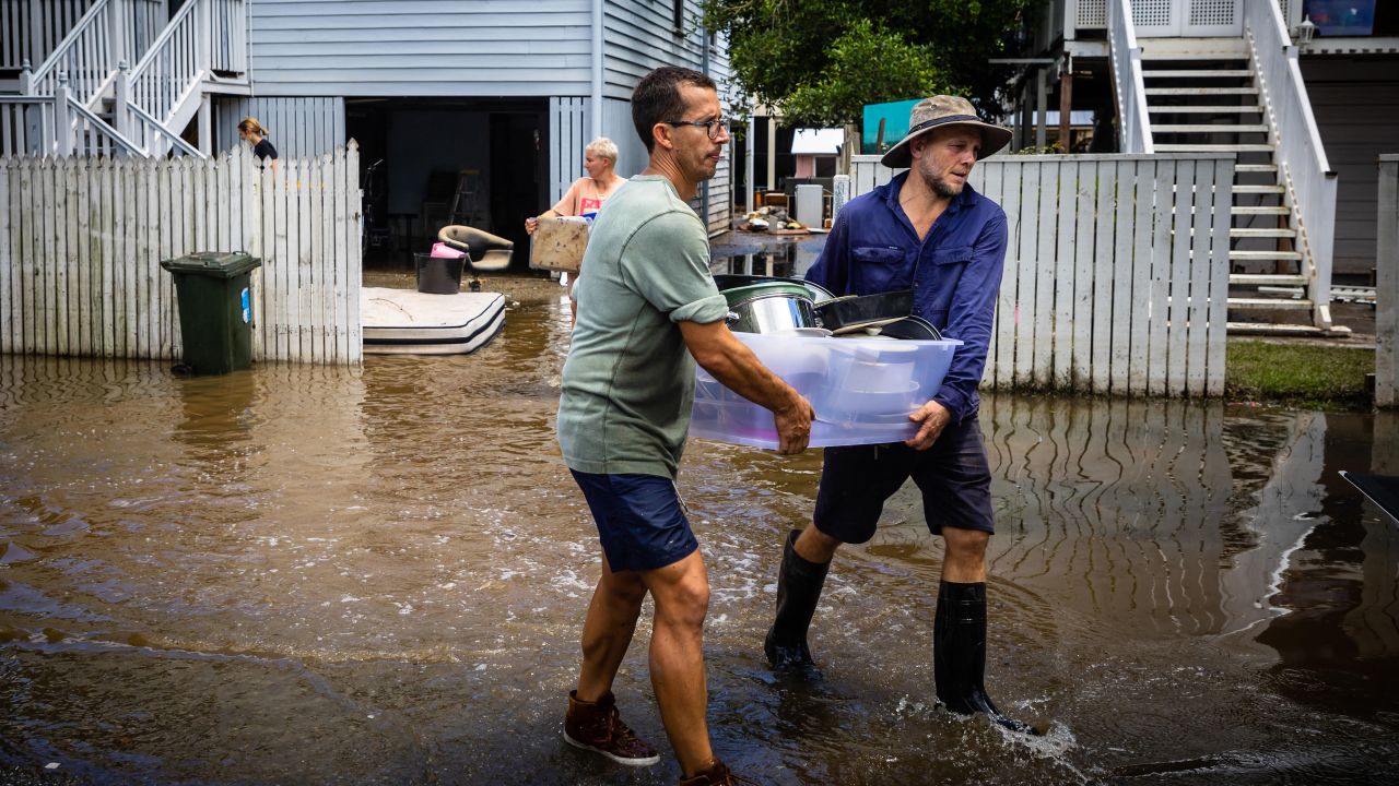 Residents carry belongings as they clean their homes in the flood-damaged suburb of Newmarket in Brisbane on March 1, 2022. 