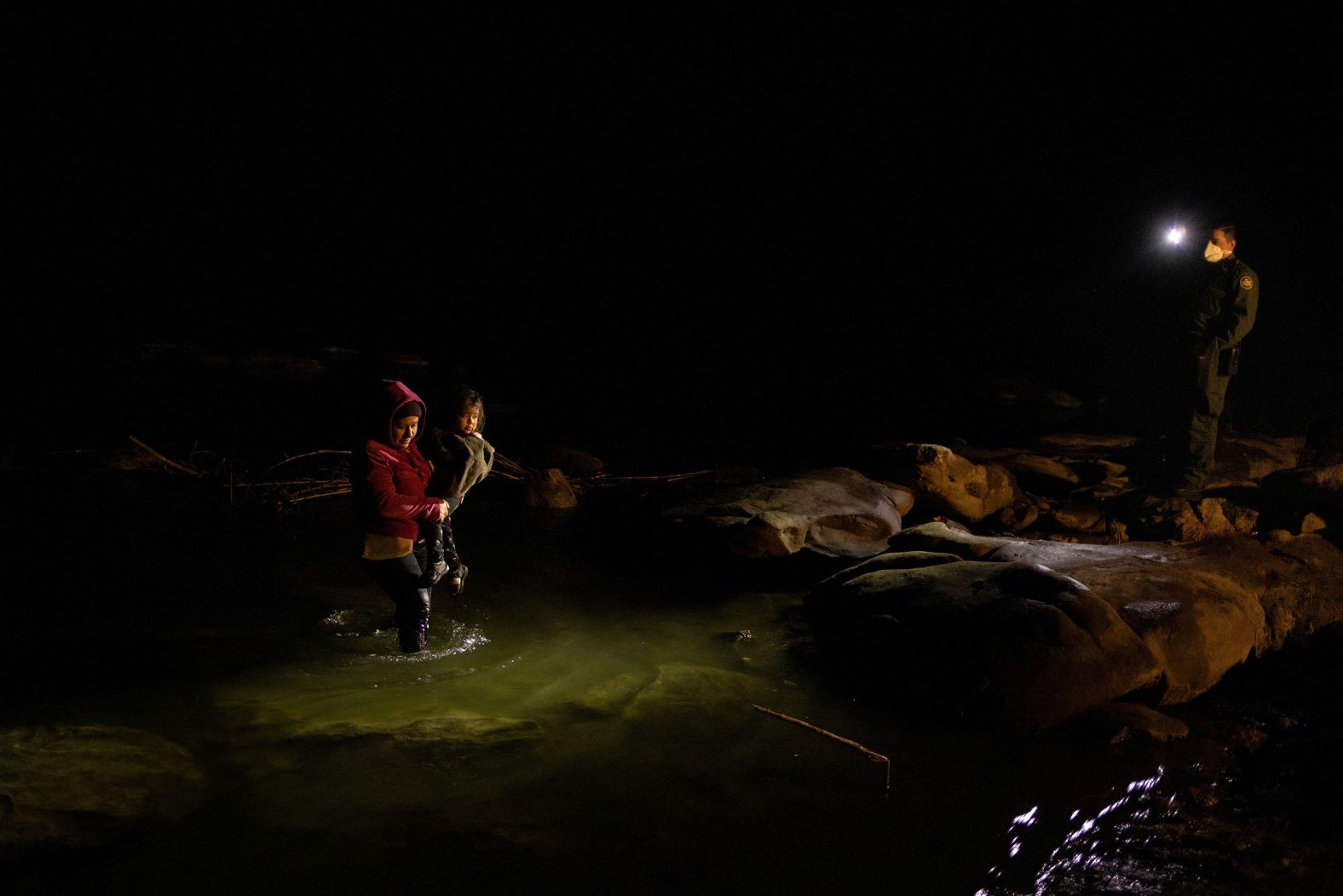 A US Border Patrol agent points his light toward Maricel, a migrant from El Salvador, as she wades across the Rio Grande in Texas with her 2-year-old daughter, Melanie, on Tuesday, March 1.