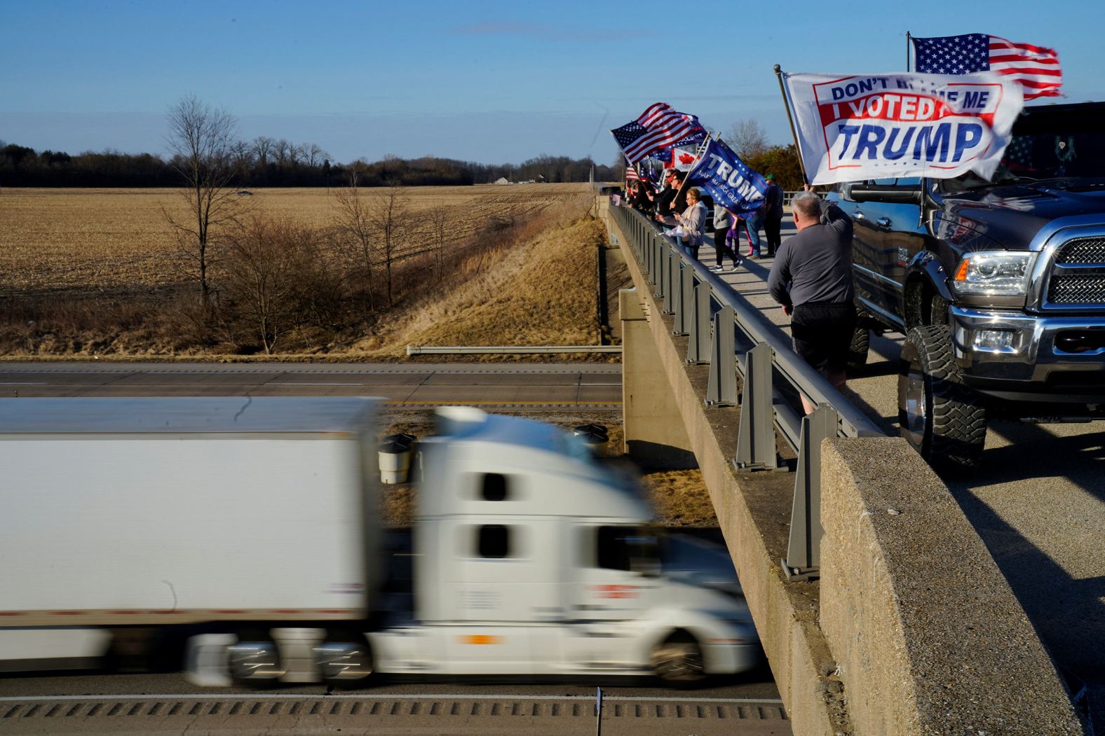 People wave flags from an overpass in Brazil, Indiana, on Tuesday, March 1, to show their support for a convoy that was heading to Washington, DC, to protest Covid-19 mandates.