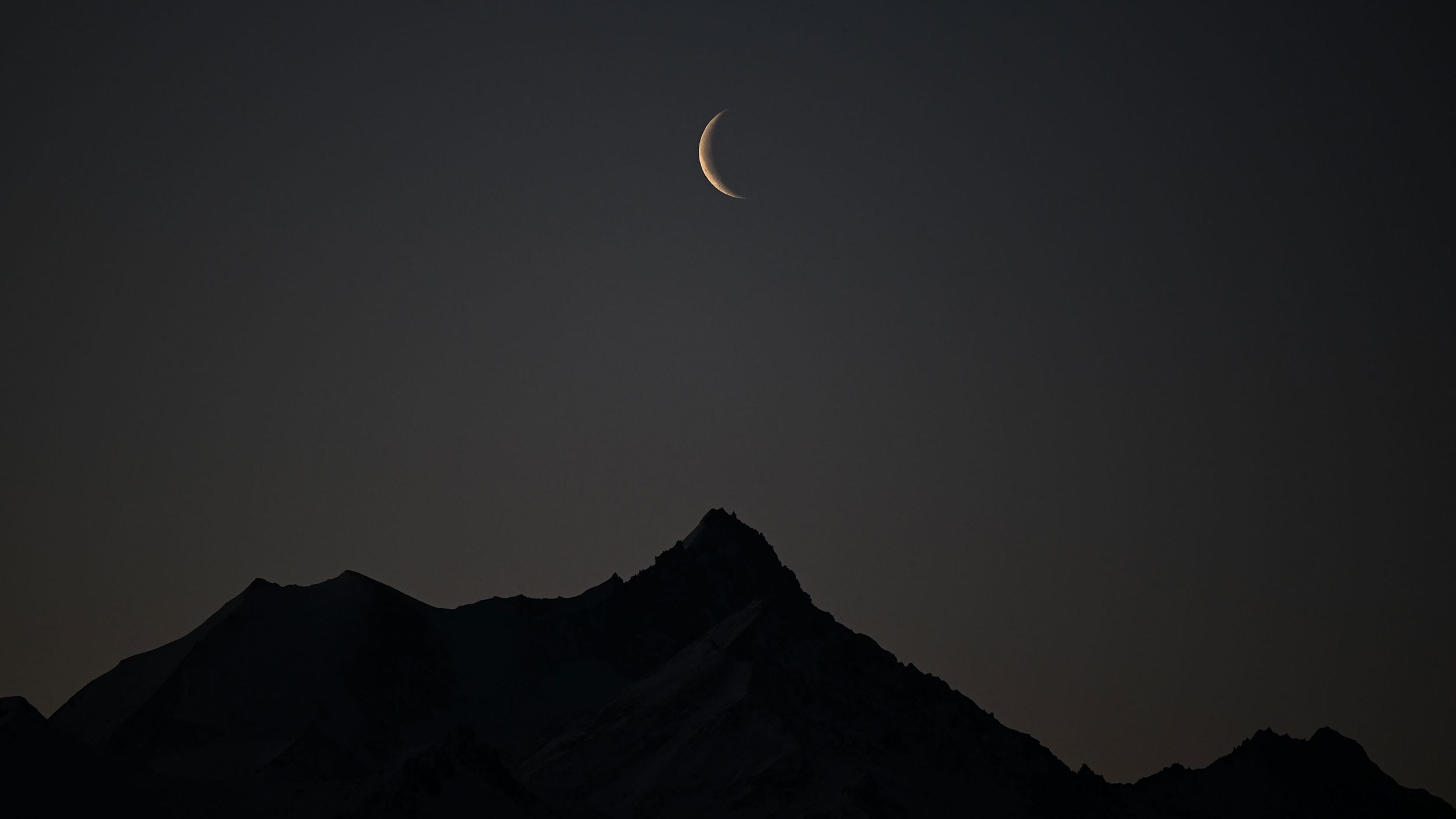A picture taken early on February 27, 2022 shows a crescent of moon above the 4506 meters high Weisshorn mountain in the Swiss alps from Crans-Montana, Switzerland. 