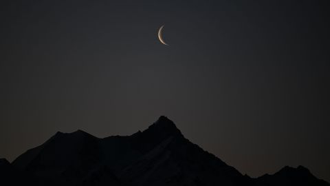 A picture taken early on February 27, 2022 shows a crescent of moon above the 4506 meters high Weisshorn mountain in the Swiss alps from Crans-Montana, Switzerland.