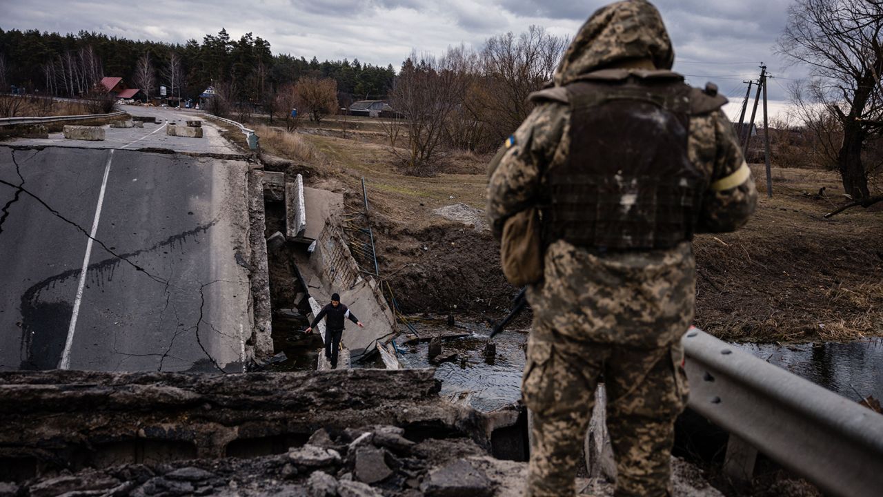A Ukrainian serviceman looks at a civilian crossing a blown up bridge in a village, east of the town of Brovary on March 6.