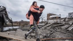 A man carries a woman as they cross an improvised path while fleeing the town of Irpin, Ukraine, Sunday, March 6, 2022. In Irpin, near Kyiv, a sea of people on foot and even in wheelbarrows trudged over the remains of a destroyed bridge to cross a river and leave the city. (AP Photo/Oleksandr Ratushniak)