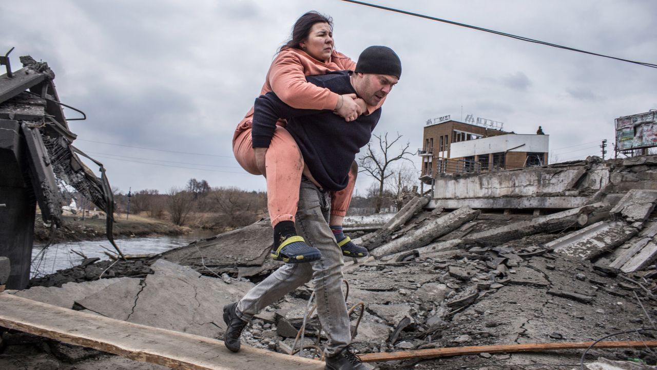A man carries a woman as they cross an improvised path to flee the town of Irpin, near Kyiv.