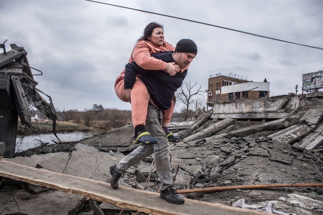 A man carries a woman as they cross an improvised path while fleeing Irpin, Ukraine on Sunday.