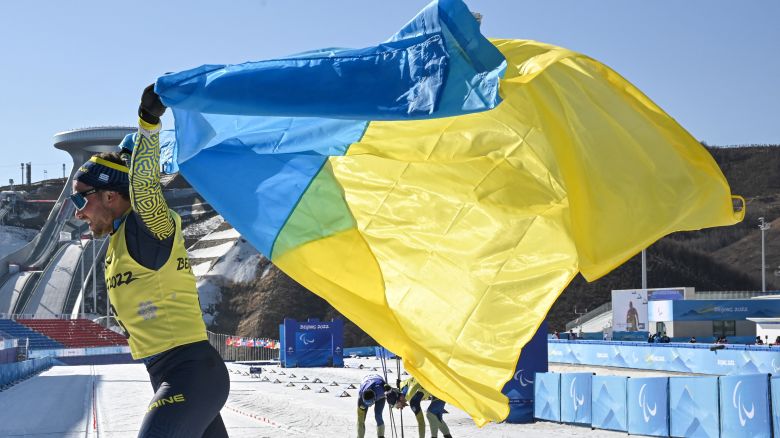 A guide for the Ukraine team celebrates with his country's flag after winning the mens middle distance vision impaired para biathlon final event on March 8, 2022, at the Zhangjiakou National Biathlon Centre during the Beijing 2022 Winter Paralympic Games. (Photo by Mohd Rasfan / AFP) (Photo by MOHD RASFAN/AFP via Getty Images)