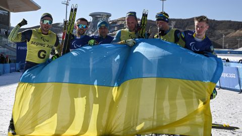 Ukrainian athletes celebrate with their country's flag after winning the mens middle distance vision impaired para biathlon.