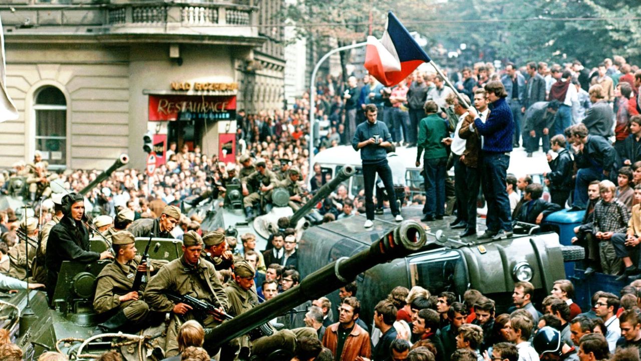 Czech demonstrators hold flags atop an overturned truck as other Prague residents surround Soviet tanks in  Prague, August, 1968.