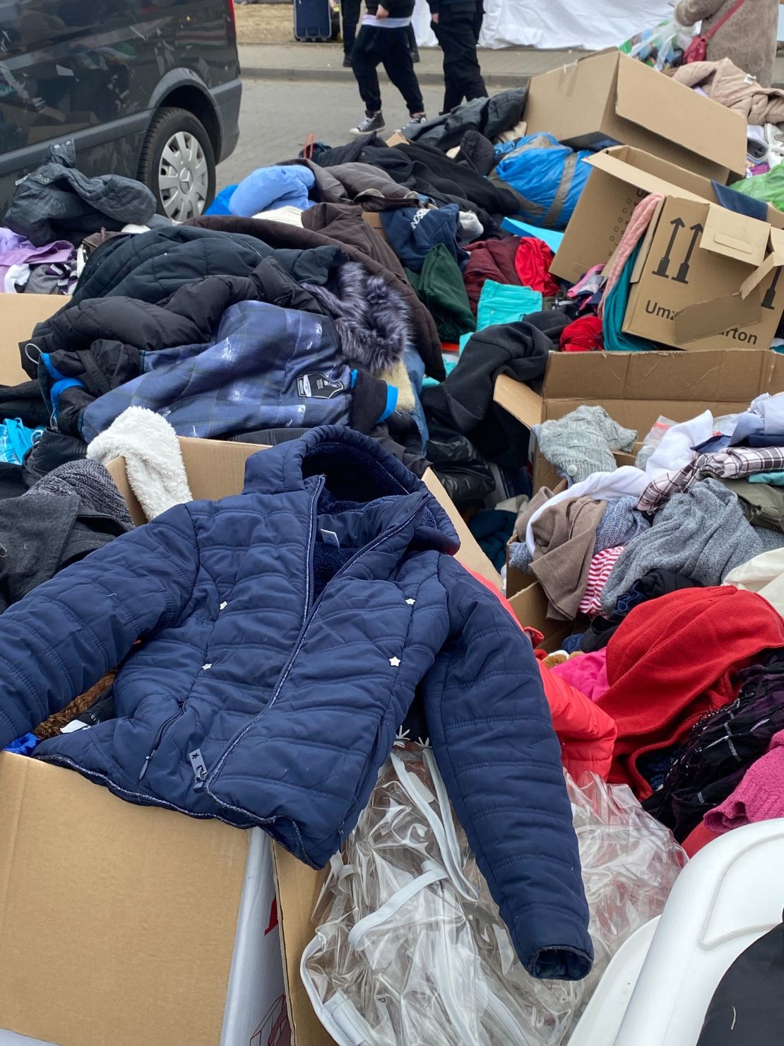 Small mountains of clothing, shoes, jackets and outerwear fill cardboard boxes just outside of the Przemyśl train station at a refugee relocation center.