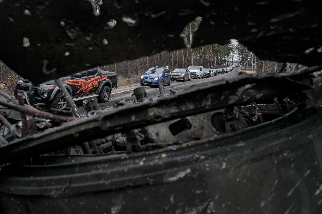 Cars drive past a destroyed Russian tank as civilians leave Irpin on March 9. A Ukrainian official said lines of vehicles <a target=