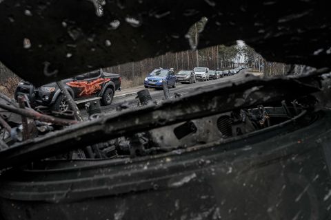 Cars drive past a destroyed Russian tank as civilians leave Irpin on March 9. A Ukrainian official said lines of vehicles stretched for miles as people tried to escape fighting in districts to the north and northwest of Kyiv.